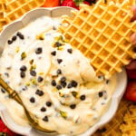 A pizzelle cookie dipping into a bowl of cannoli dip.