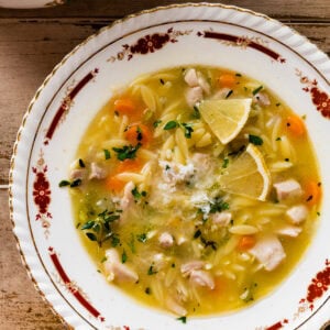 Lemon Chicken Orzo Soup in an old fashioned soup bowl with a little cheese on top. Spoon in bowl ready to take a bite.