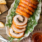 Partially-sliced porchetta on a platter with rosemary sprigs.