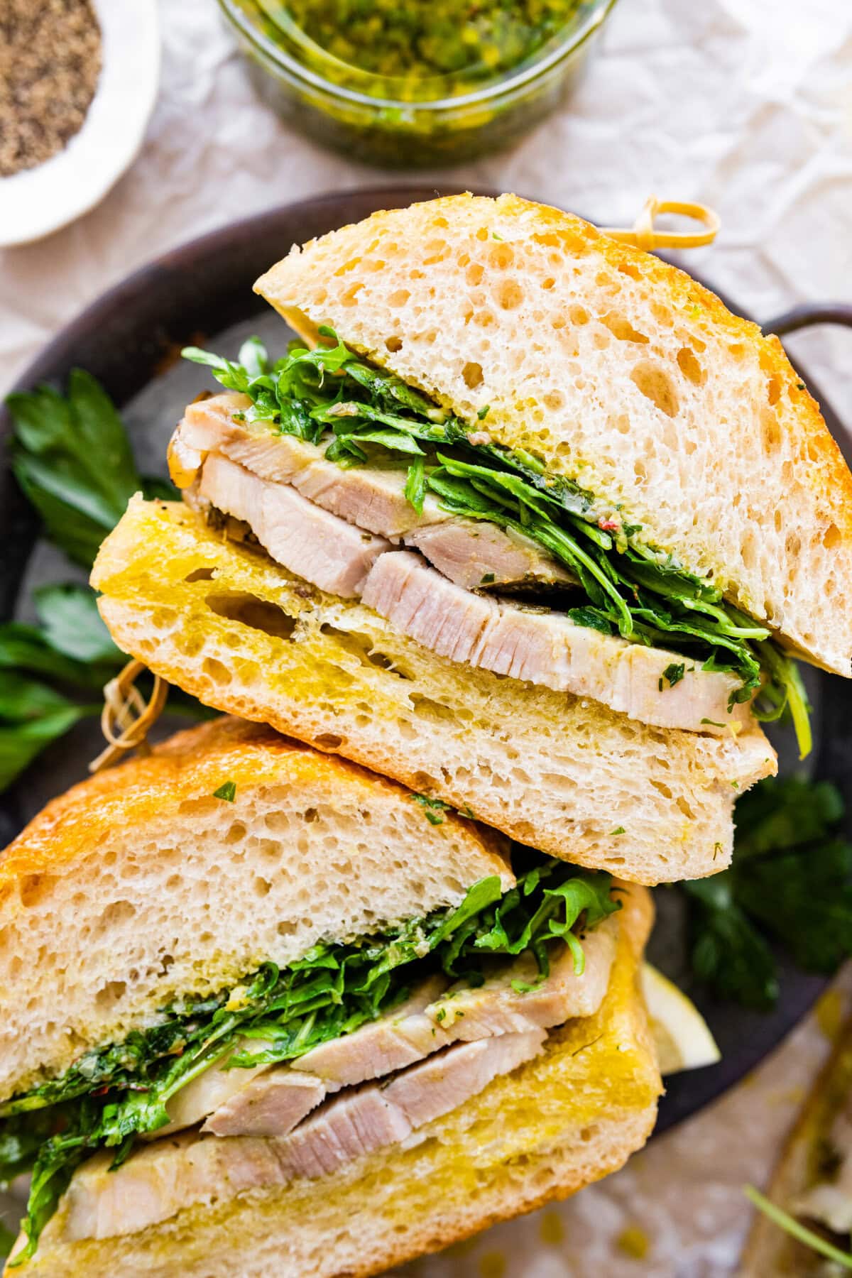 porchetta sandwich with Italian Salsa Verde on the side. The sandwiches are on a metal serving platter.