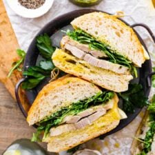 porchetta sandwich with Italian Salsa Verde on the side. The sandwiches are on a metal serving platter.
