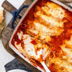 Baked Spinach and ricotta manicotti in a beautiful casserole dish. Fresh parmigiano cheese on the side. Serving spoon taking out a portion.