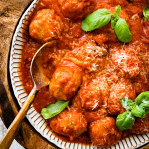 cooked Italian turkey meatballs recipe on a serving platter with a spoon to serve. Basil as garnish. Freshly grated parmigiano cheese as garnish.