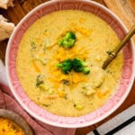 Broccoli cheddar soup recipe in a pink bowl with a spoon in it ready to serve.