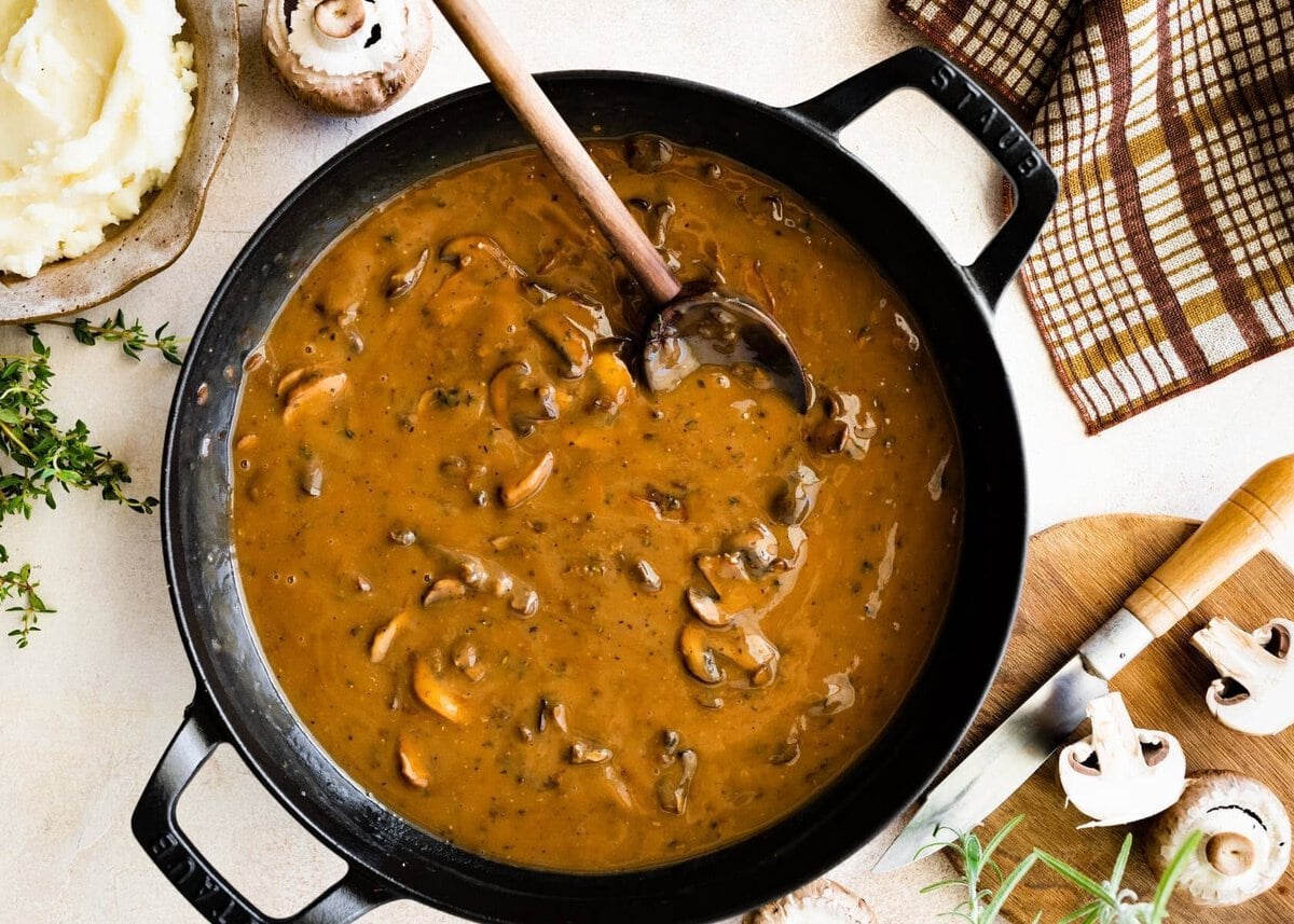 Easy mushroom gravy in a skillet pan with wooden spoon. Mushrooms on the side.