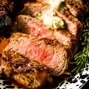 Sliced broiled New York Steak on a platter. One steak is cut into slices and there is a butter sauce pored over the top.