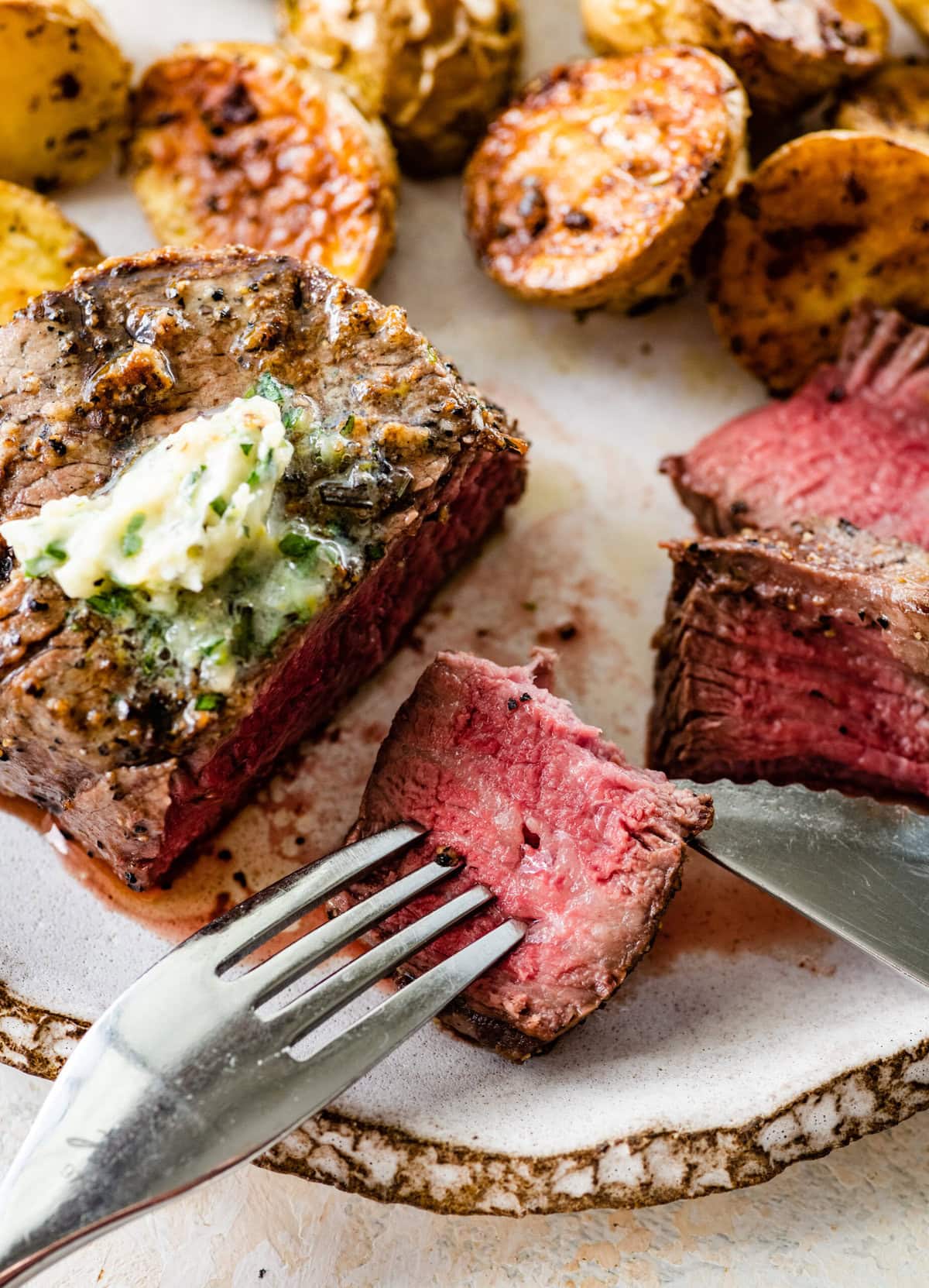 Slice grilled filet mignon on the plate with a medium rare look. Cut piece of the meat on a fork ready to eat.