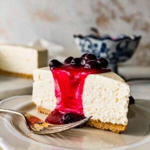 A slice of Italian cheesecake with blueberry sauce on top and a fork to the side.