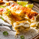 White chicken enchilada on a plate with a fork. Limes on the side and ready to eat. A bite taken out of the enchiladas with a fork.