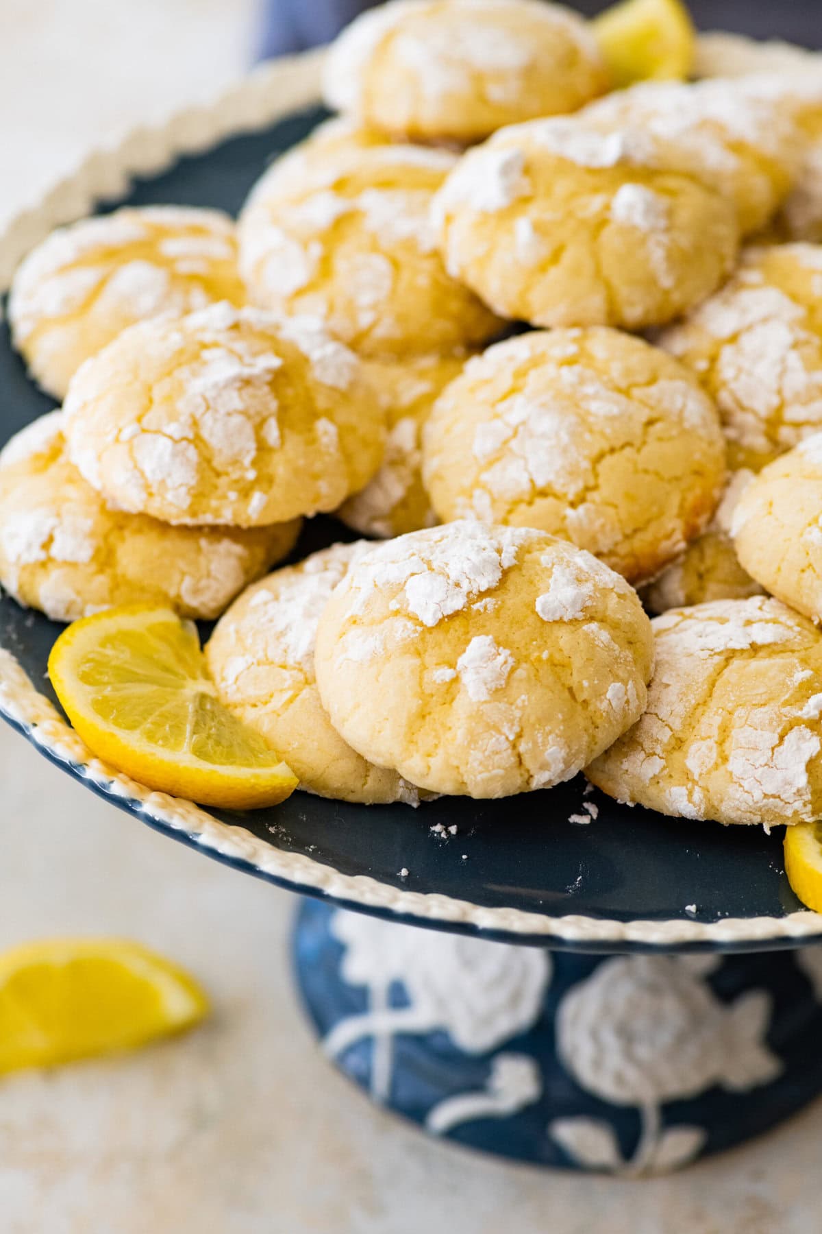 finished lemon crinkle cookies on a white and blue cake platter ready for serving. Lemon slices decorating the plate.