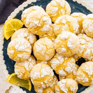 finished lemon crinkle cookies on a white and blue cake platter ready for serving. Lemon slices decorating the plate. Downward view.