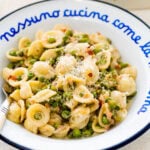 a blue and white Italian style plate with a portion of the creamy pasta with pancetta and peas. Extra cheese and red pepper flakes on top. Close up of the plate with the pasta.