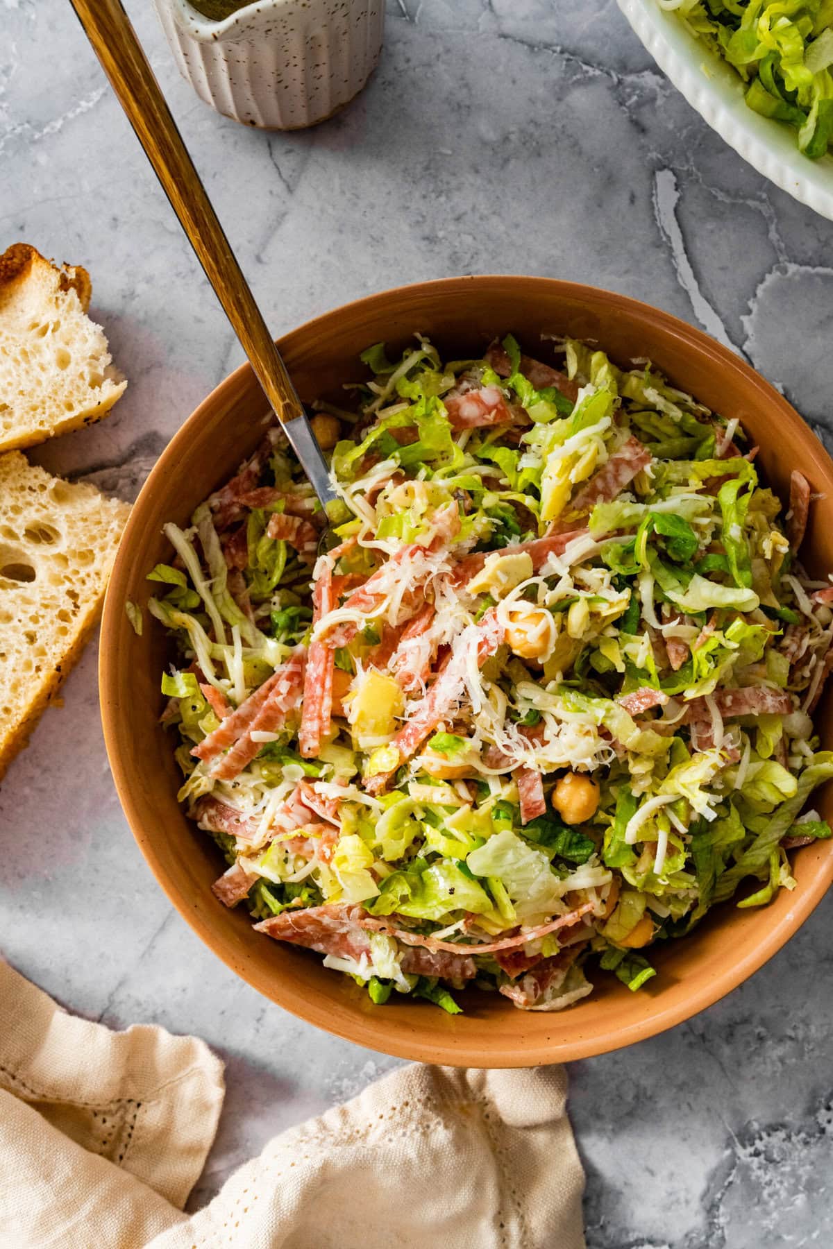 Famous La Scala chopped salad in a small wooden serving bowl with a fork. Extra dressing on the side. Focaccia bread on the side.