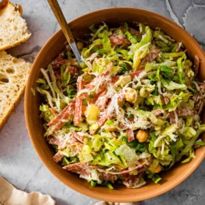 Famous La Scala chopped salad in a small wooden serving bowl with a fork. Extra dressing on the side. Focaccia bread for serving.