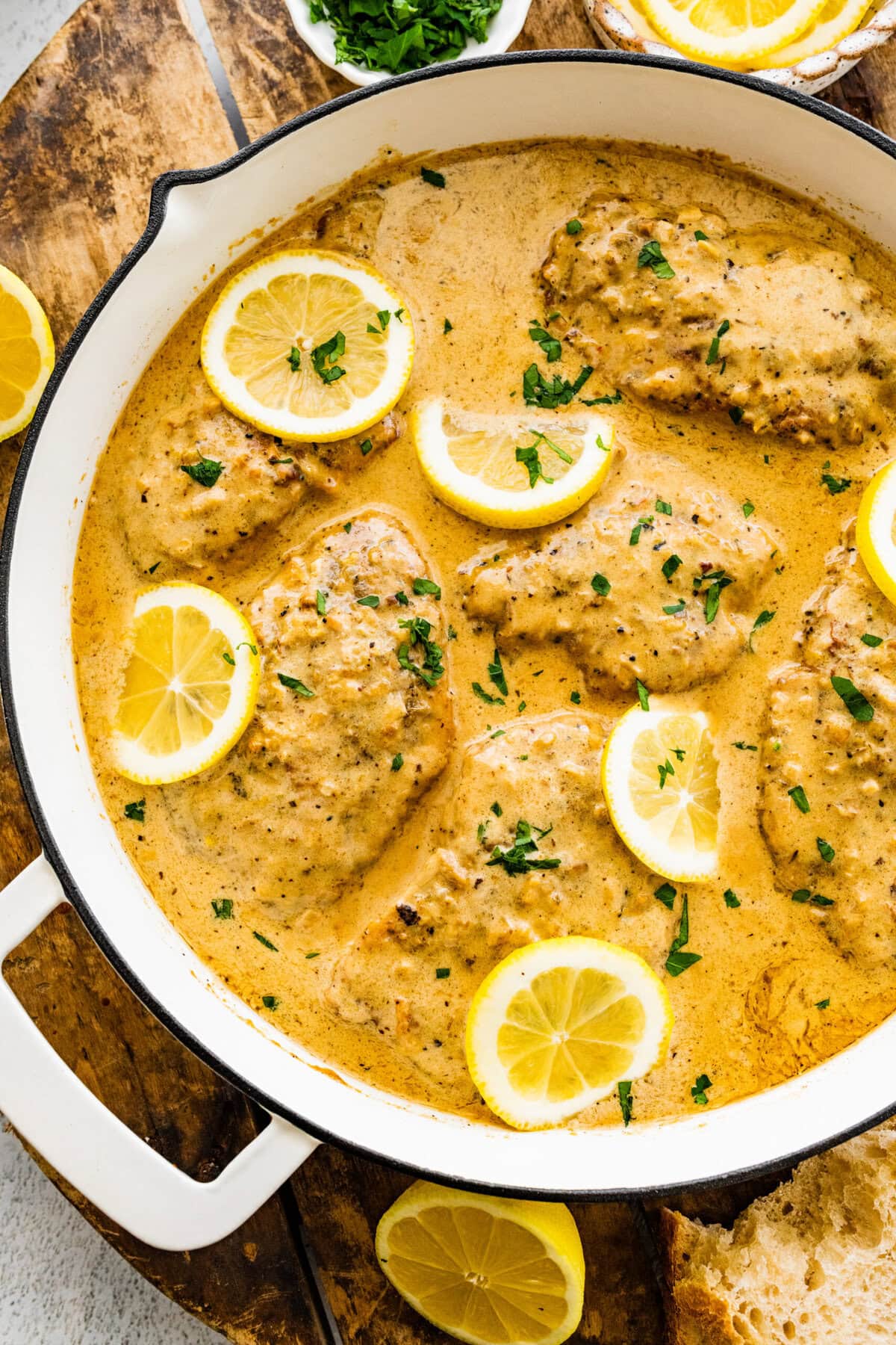 pan with creamy lemon chicken with fresh parsley and lemon slices in the pan.