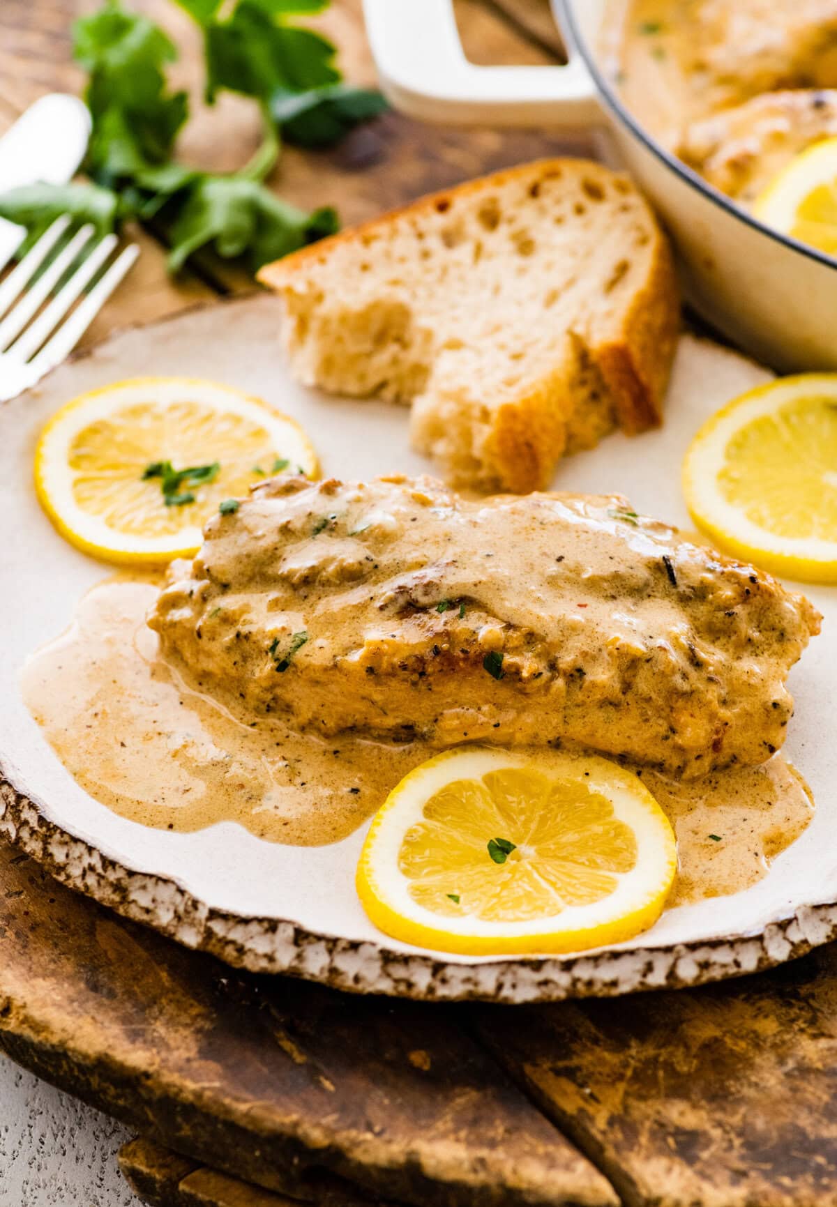 Creamy lemon chicken on a white plate with crusty bread on the side.