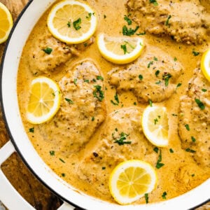 pan with creamy lemon chicken with fresh parsley and lemon slices in the pan.