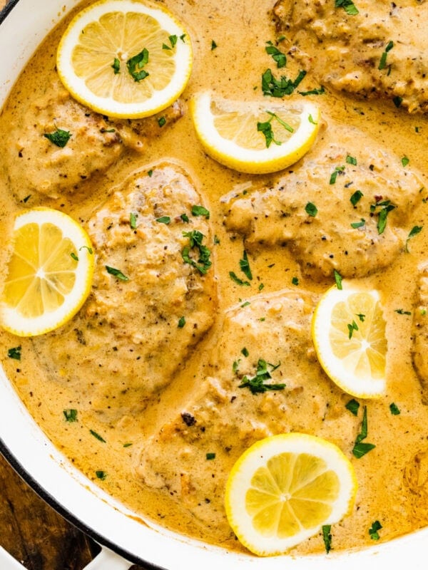 pan with creamy lemon chicken with fresh parsley and lemon slices in the pan.