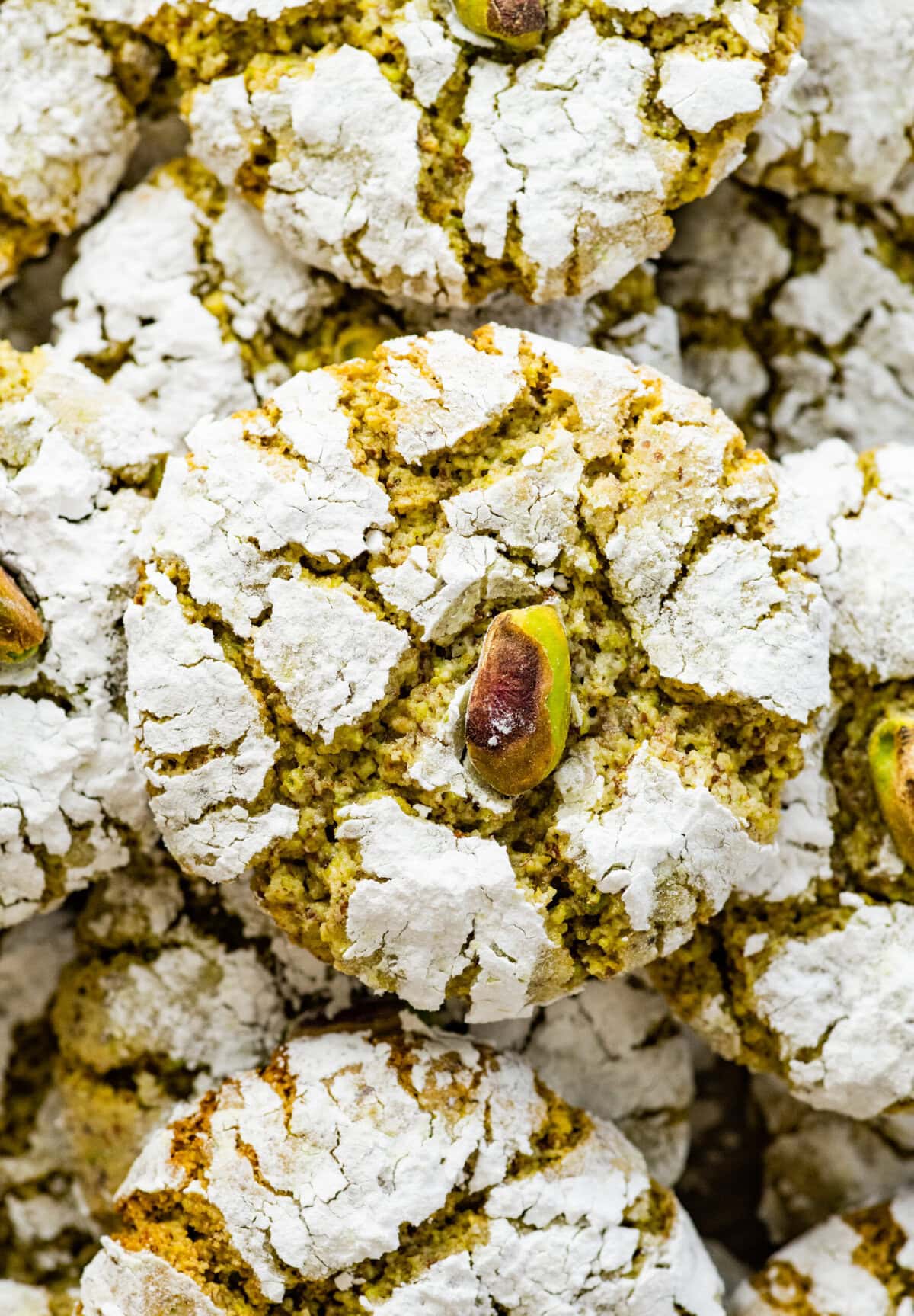 Italian pistachio cookies stacked on a plate. You can see the crinkle from the powdered sugar and the vibrant green color.