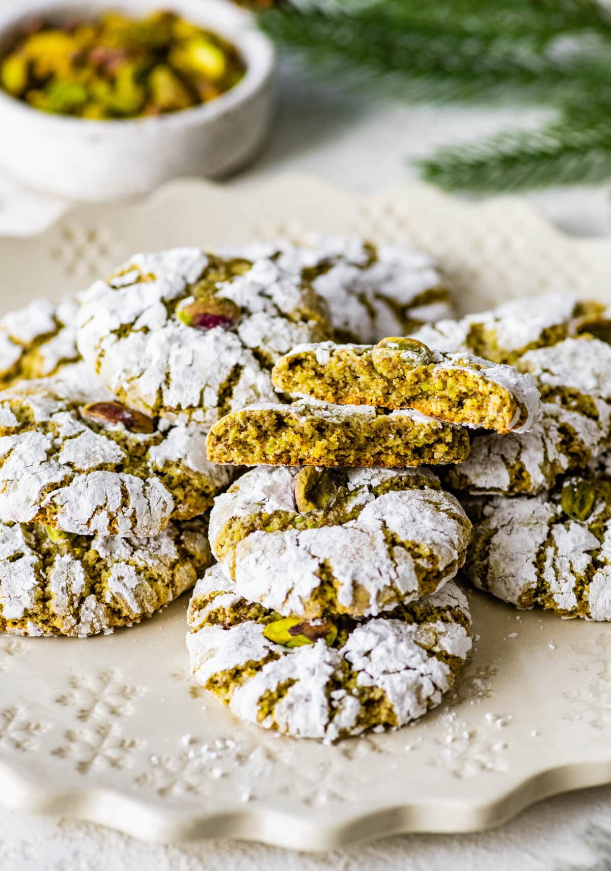 Italian pistachio cookies stacked on a plate. One cookie is broken in half to see the inside.