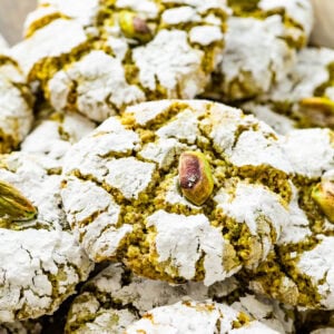 Italian pistachio cookies stacked on a plate. You can see the crinkle from the powdered sugar and the vibrant green color.