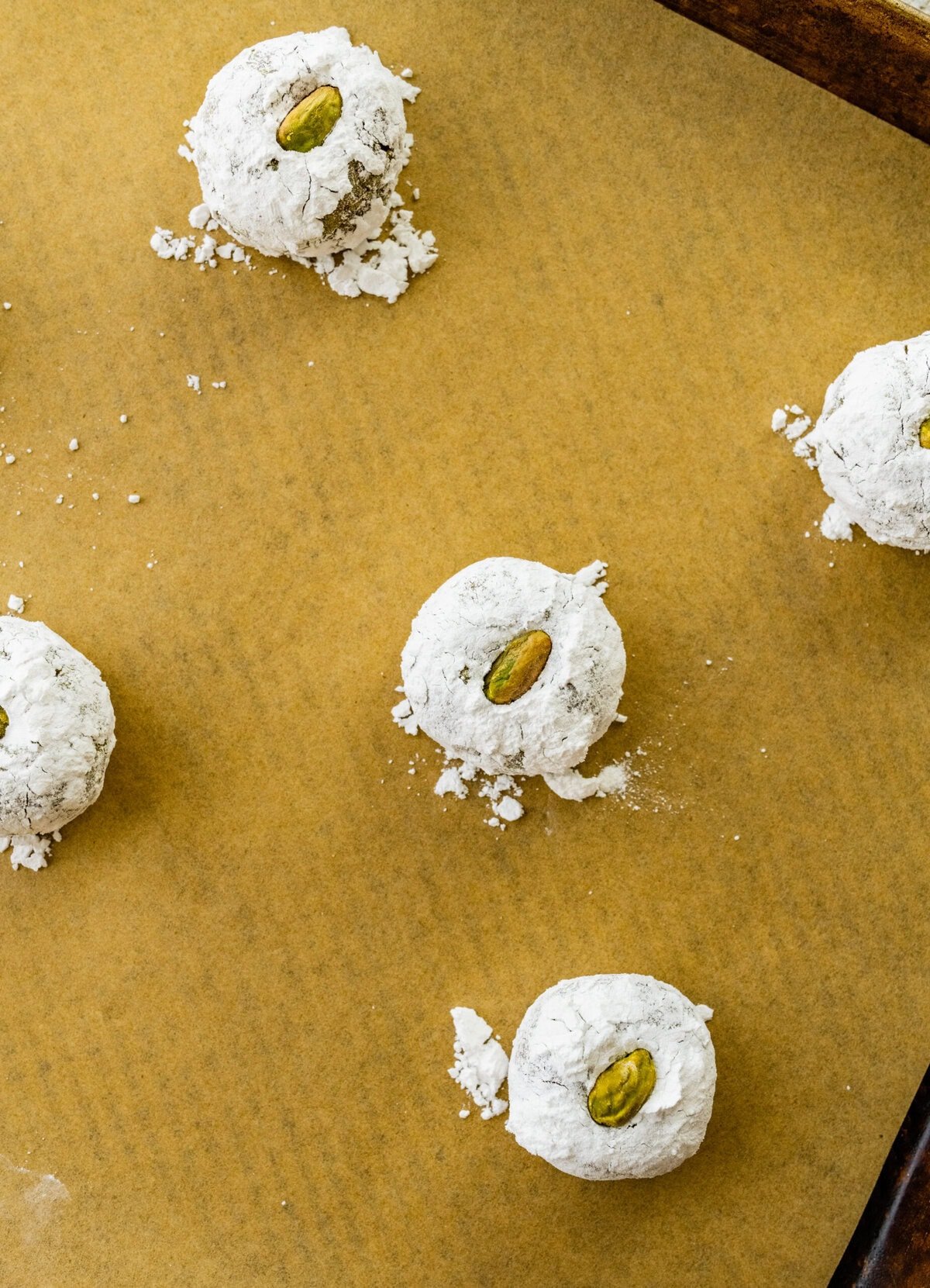 Making Italian Pistachio Cookies- place the powdered sugar pistachio cookie dough balls on a lined baking sheet with a pistachio at the center.