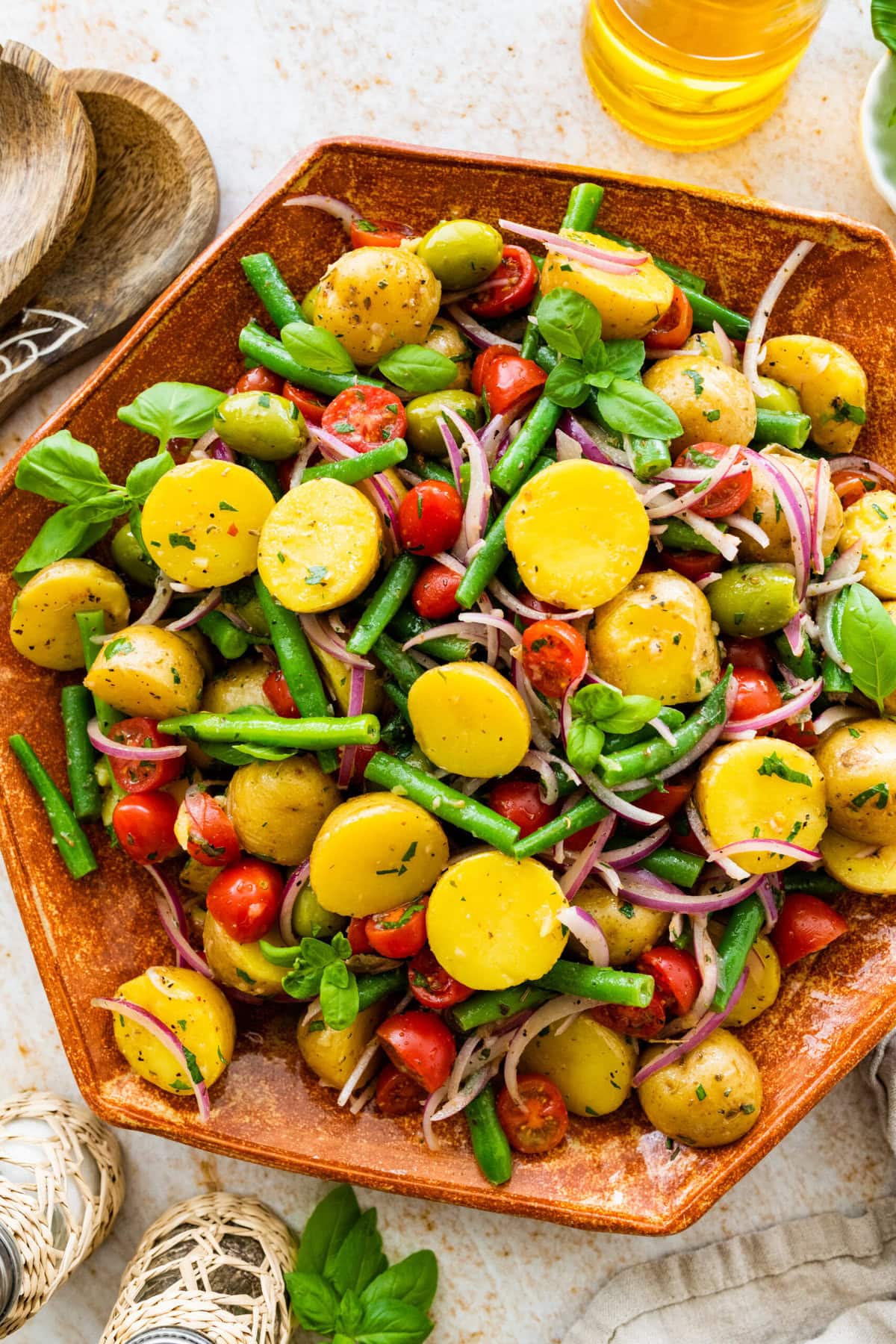 Close up of Italian potato salad in a wooden serving platter with wooden servers on the side.