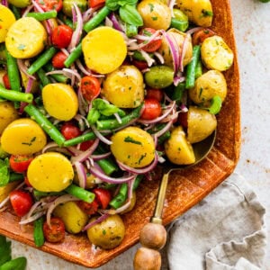 Italian potato salad in a wooden serving platter with wooden servers on the side.