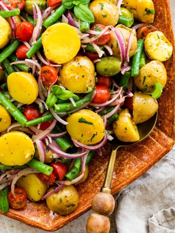 Italian potato salad in a wooden serving platter with wooden servers on the side.
