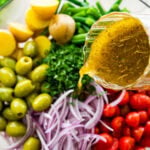 pouring zest Italian dressing over a potato salad.