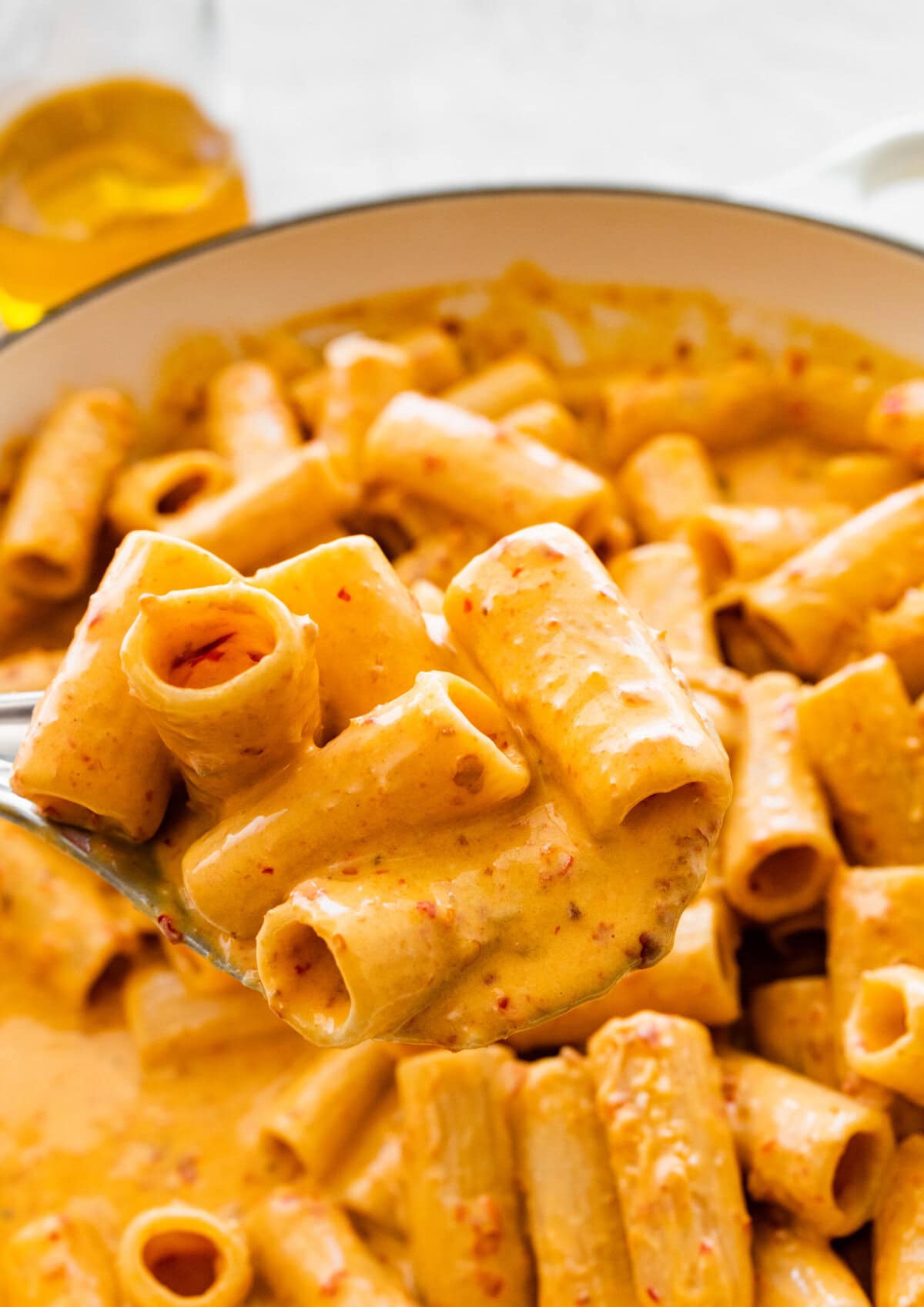 Nduja pasta sauce and pasta in a serving dish Large spoon holding one serving of pasta.