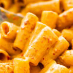Nduja pasta sauce and pasta in a serving dish Large spoon holding one serving of pasta.