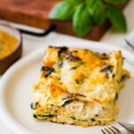 slice of white chicken lasagna on a plate with a fork and knife.