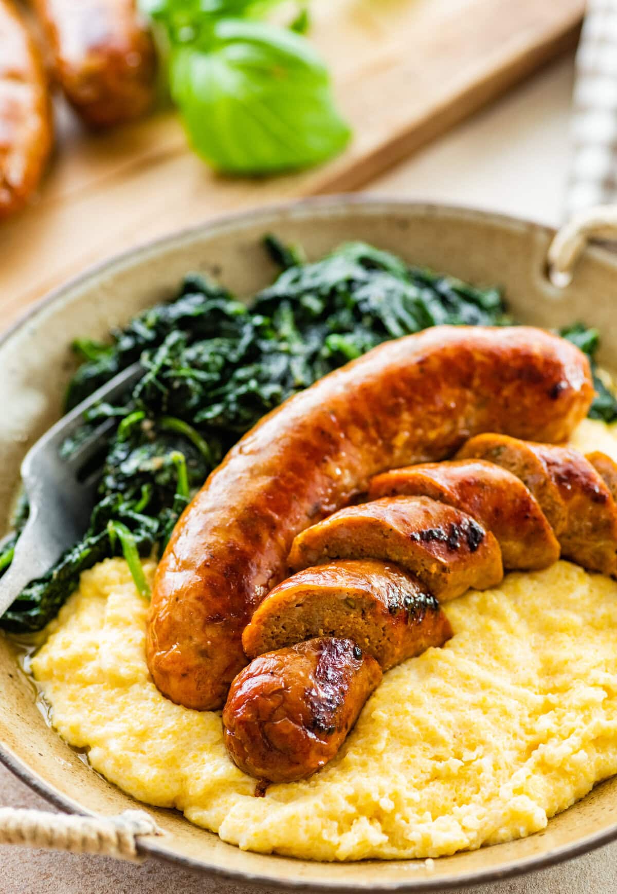 Italian baked sausage in a bowl with polenta and cooked greens. Sausage is cut into slices.