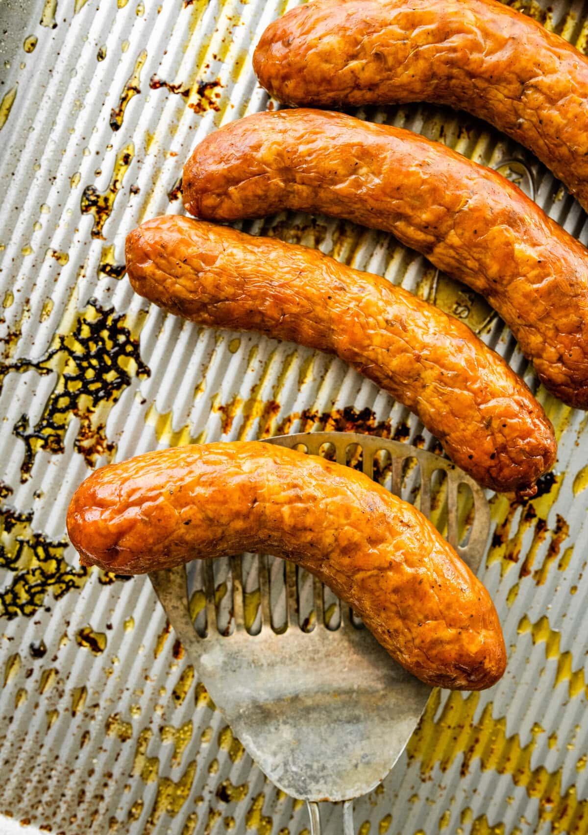 Italian sausage on a baking sheet with a spatula lifting one.