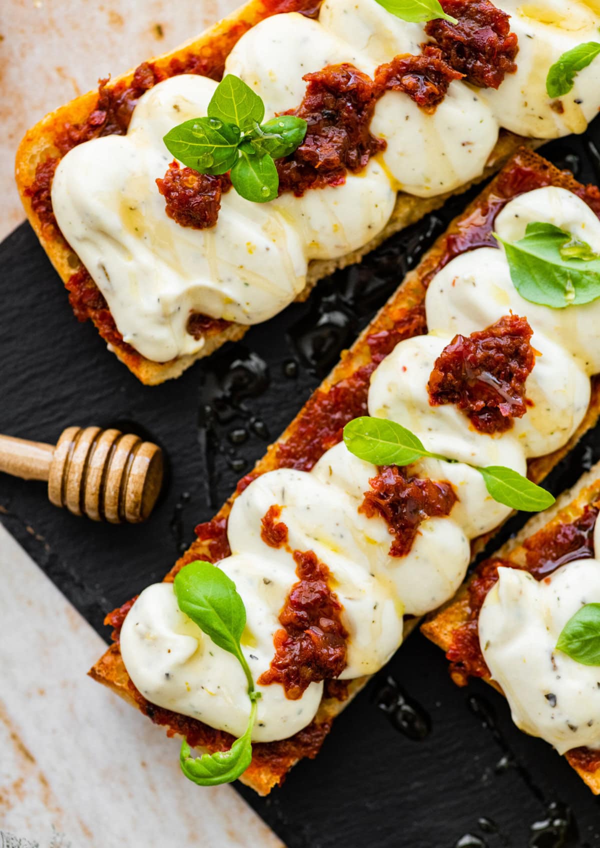 nduja ricotta toast on a black platter with honey drizzle and basil on top as garnish.