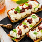 nduja ricotta toast on a black platter with honey drizzle and basil on top as garnish.