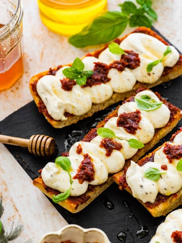 nduja ricotta toast on a black platter with honey drizzle and basil on top as garnish.
