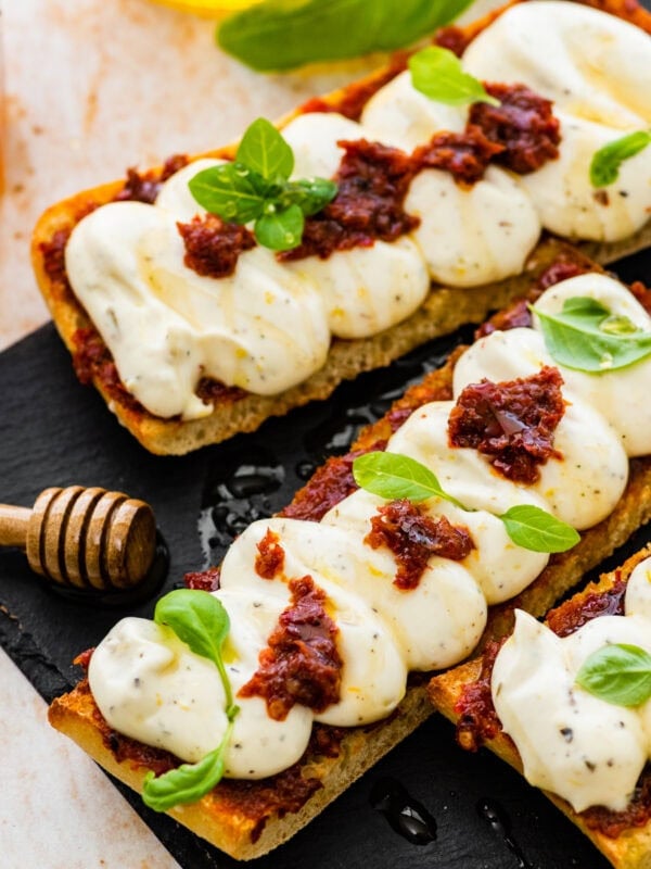 nduja ricotta toast on a black platter with honey drizzle and basil on top as garnish.