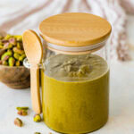 pistachio butter in a glass jar with lid and a small wooden spoon.