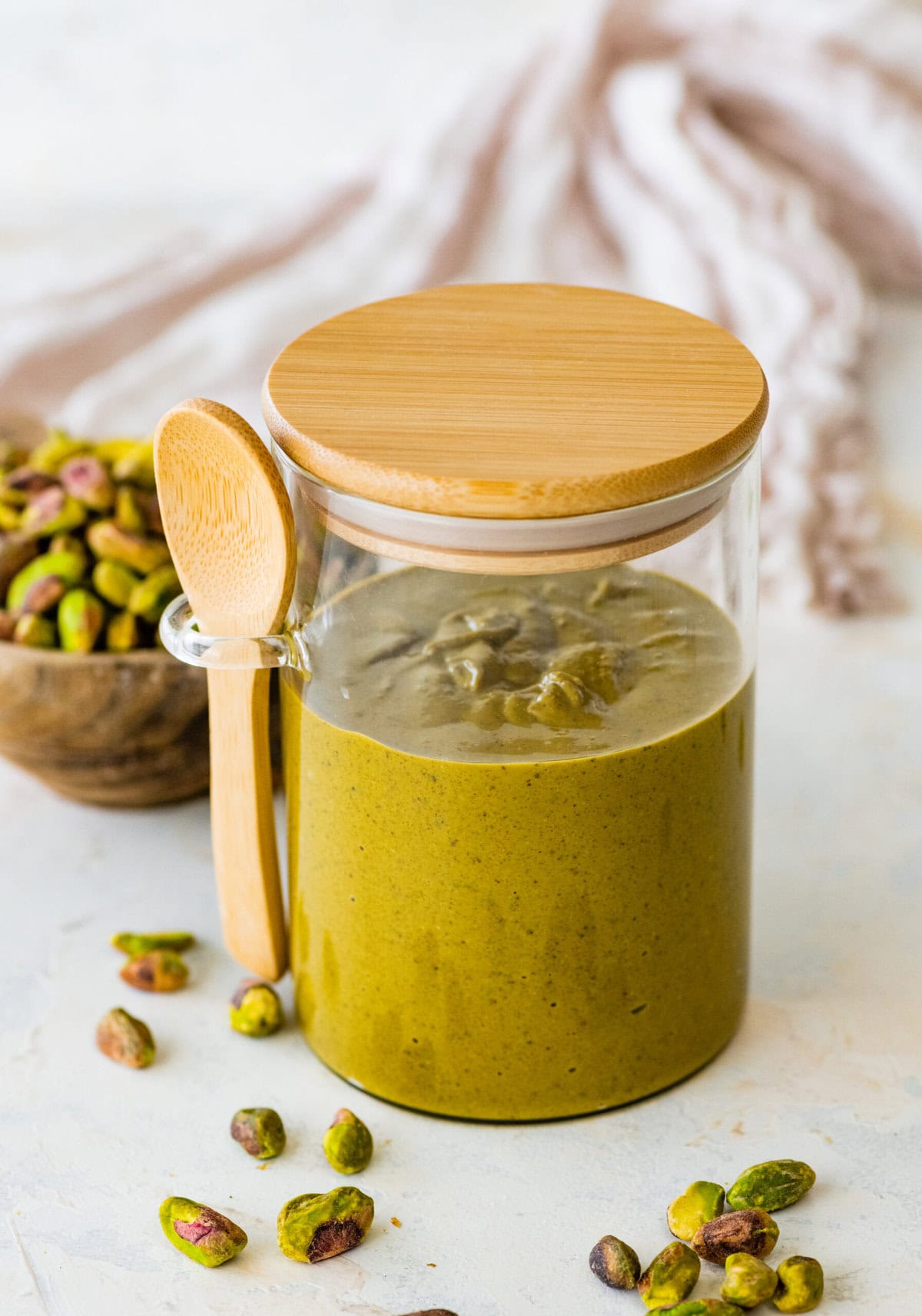 pistachio butter in a glass jar with lid and a small wooden spoon.