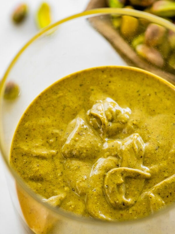 pistachio butter in a glass jar. raw pistachios in background.