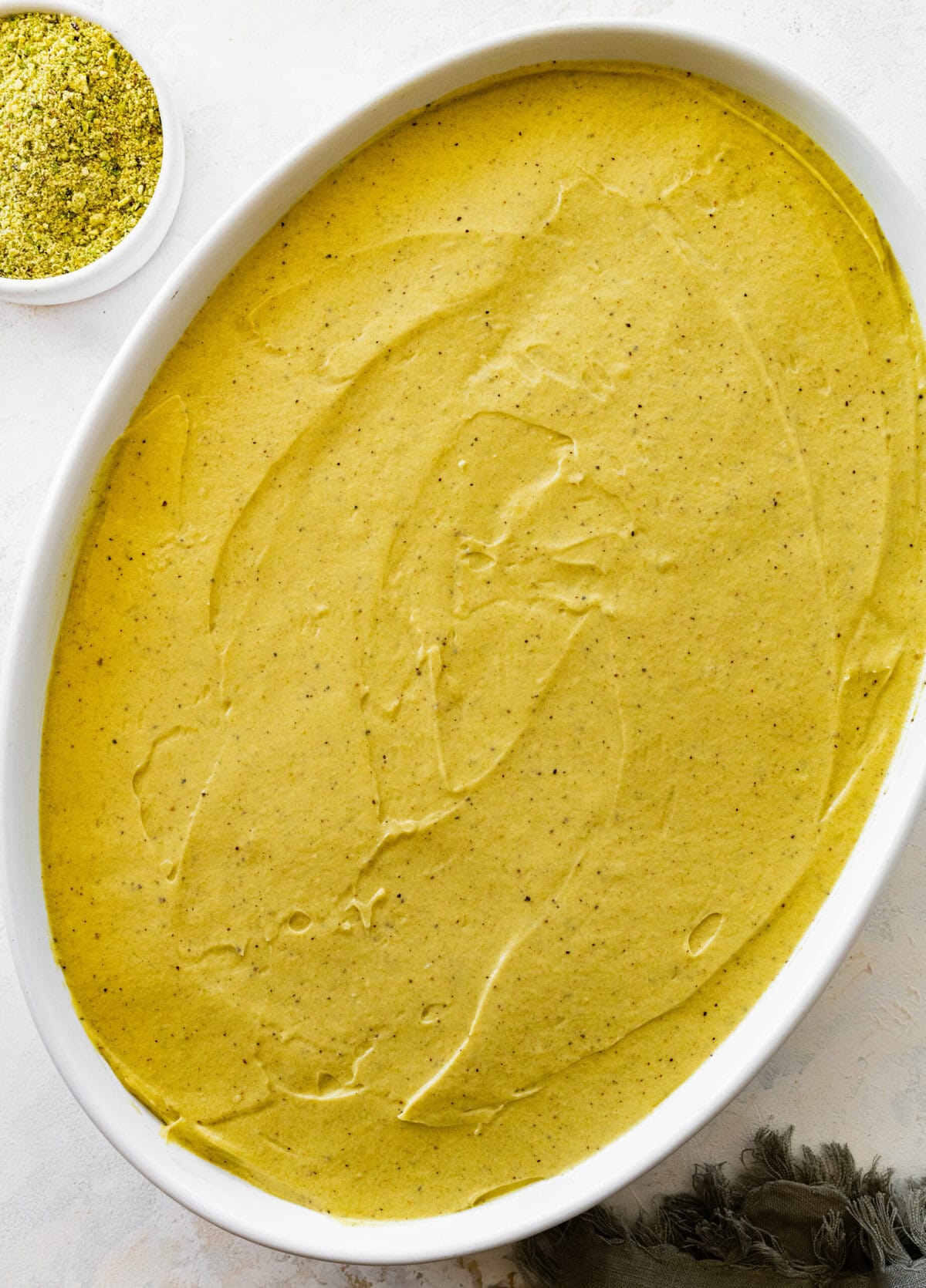 smooth creamy pistachio tiramisu in a white baking dish.
