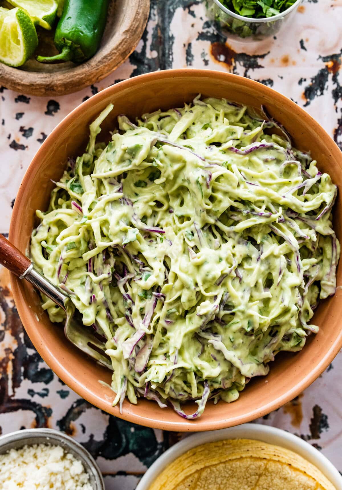 creamy avocado slaw in a bowl with a spoon in it.