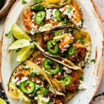 assembled shrimp tacos on a serving platter with creamy slaw and all the toppings including limes.