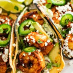 assembled shrimp tacos on a serving platter with creamy slaw and all the toppings including limes.