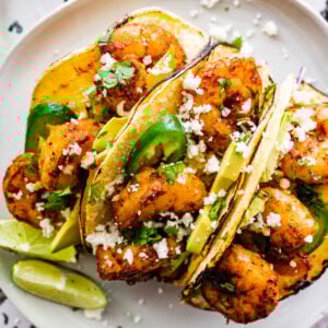 three shrimp tacos with jalapeño and lime wedges.