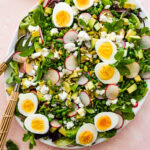 A spring salad on a platter topped with sliced eggs, herbs, and pistachios.