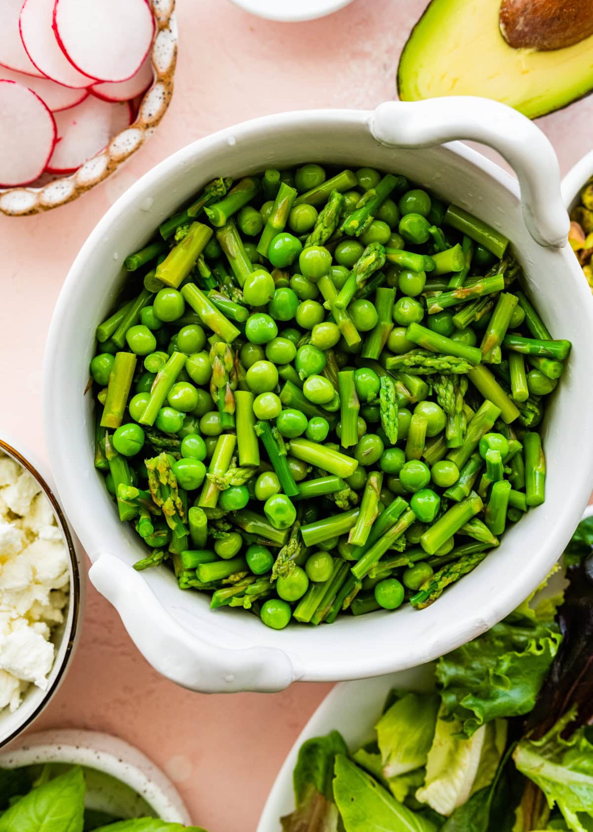 Peas and asparagus in a white bowl.