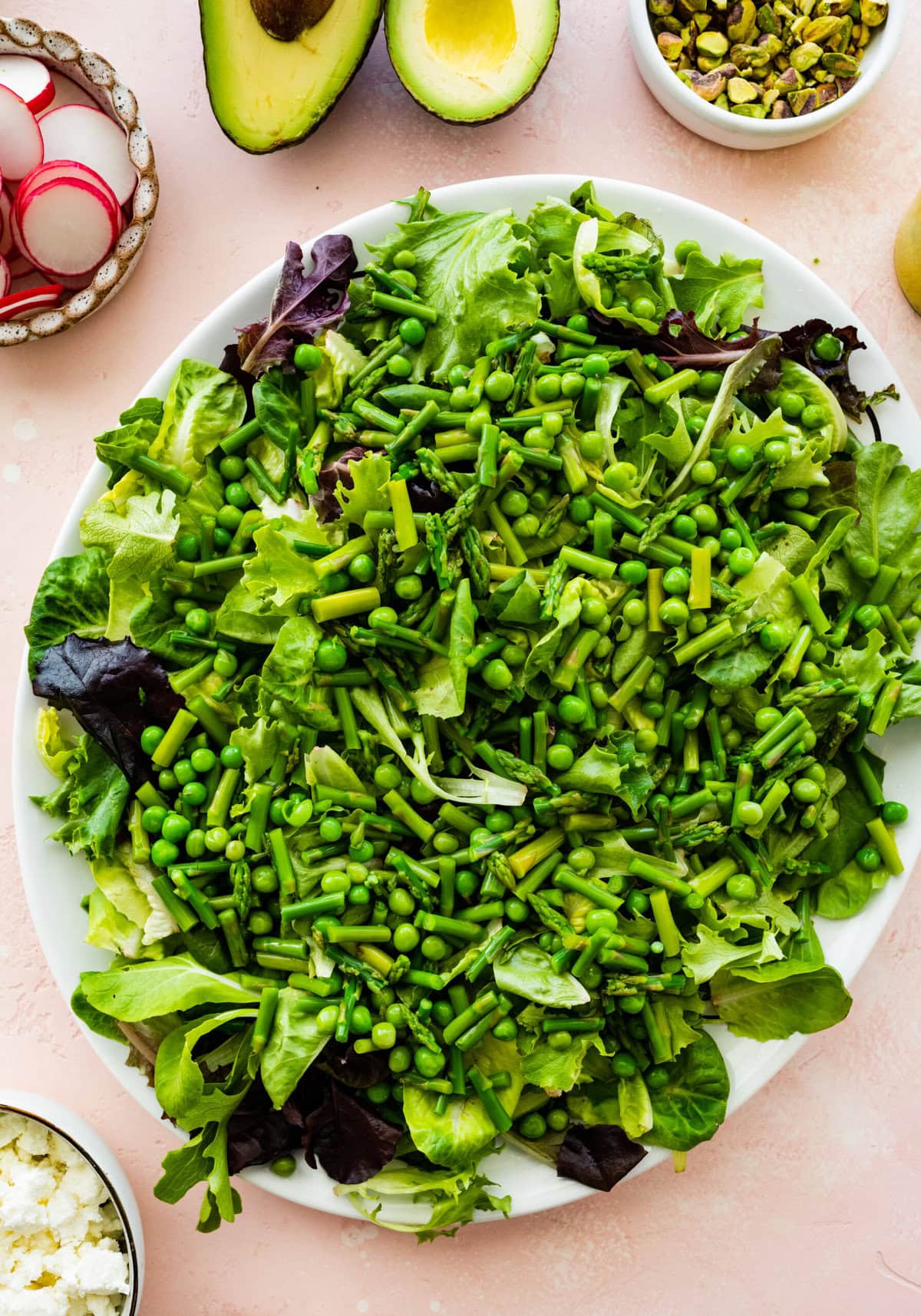 Salad mix in a large platter with peas and asparagus on top. 